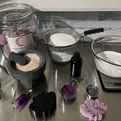Purple colored bath & body products with raw ingredients on steel table